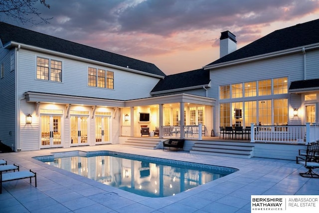 back house at dusk with a pool side deck, a patio, and french doors