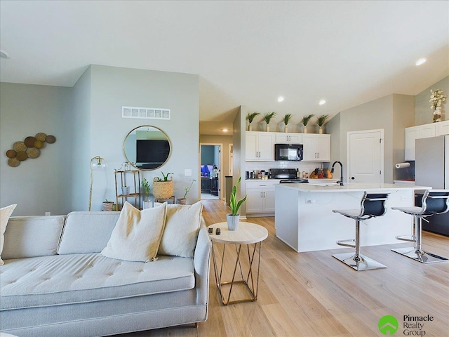 living room with recessed lighting, visible vents, light wood-style flooring, and lofted ceiling