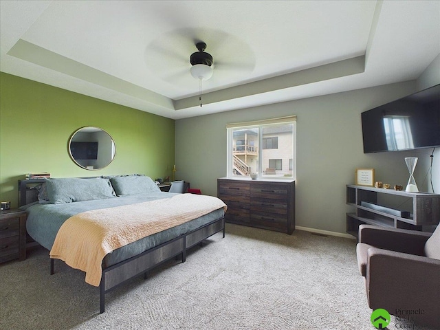 bedroom featuring a raised ceiling, light colored carpet, baseboards, and ceiling fan