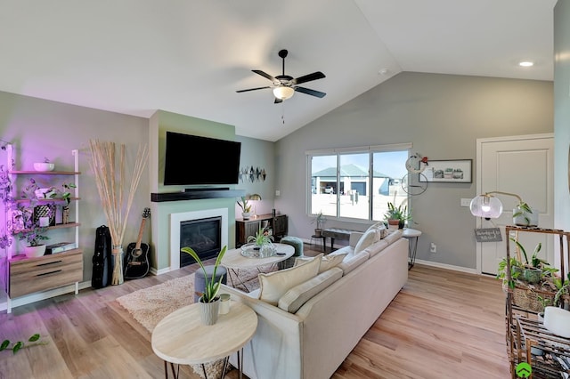 living area featuring lofted ceiling, a glass covered fireplace, a ceiling fan, and light wood finished floors