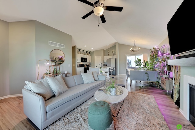 living area with visible vents, a fireplace, vaulted ceiling, ceiling fan with notable chandelier, and light wood-type flooring