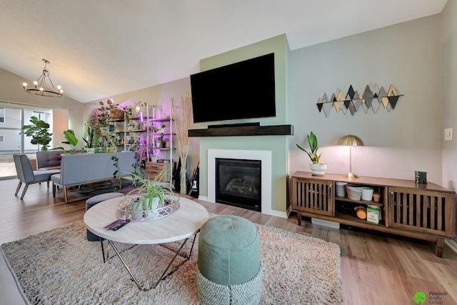 living room featuring an inviting chandelier, lofted ceiling, wood finished floors, and a glass covered fireplace