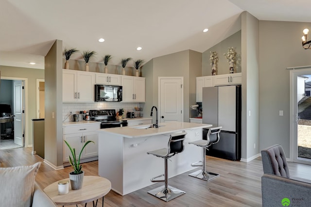 kitchen featuring an island with sink, light countertops, white cabinets, black appliances, and a sink