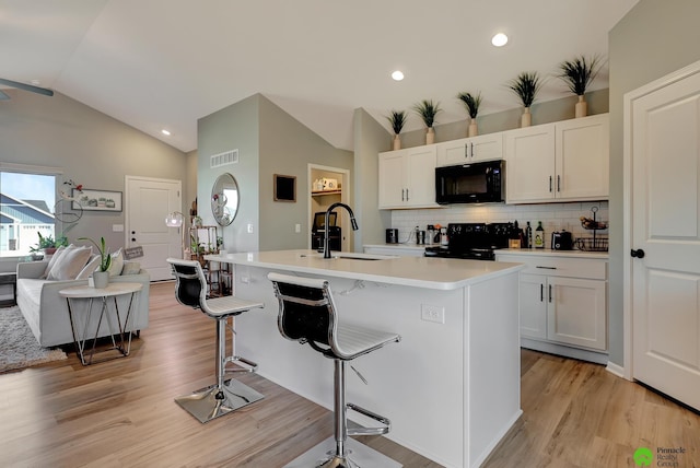 kitchen featuring visible vents, a kitchen bar, black appliances, a sink, and lofted ceiling