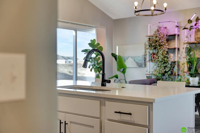 interior space featuring a notable chandelier, a sink, white cabinets, light countertops, and lofted ceiling