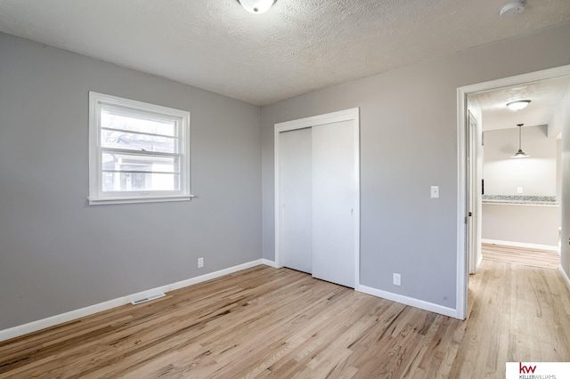 unfurnished bedroom featuring a closet, a textured ceiling, and light wood-type flooring