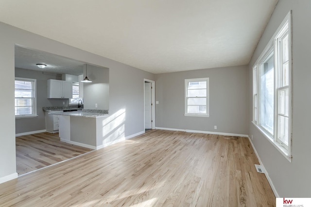 kitchen featuring light stone countertops, light wood-type flooring, sink, pendant lighting, and white cabinetry