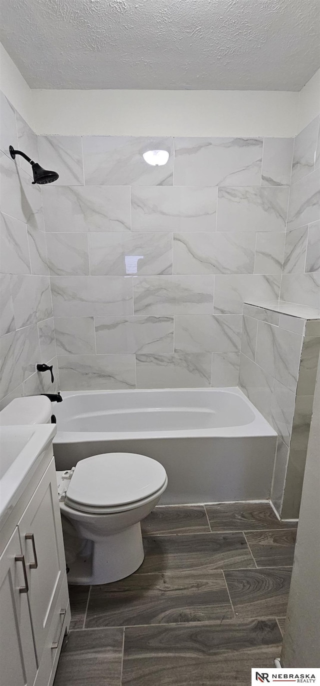 full bathroom featuring vanity, toilet, a textured ceiling, and tiled shower / bath combo