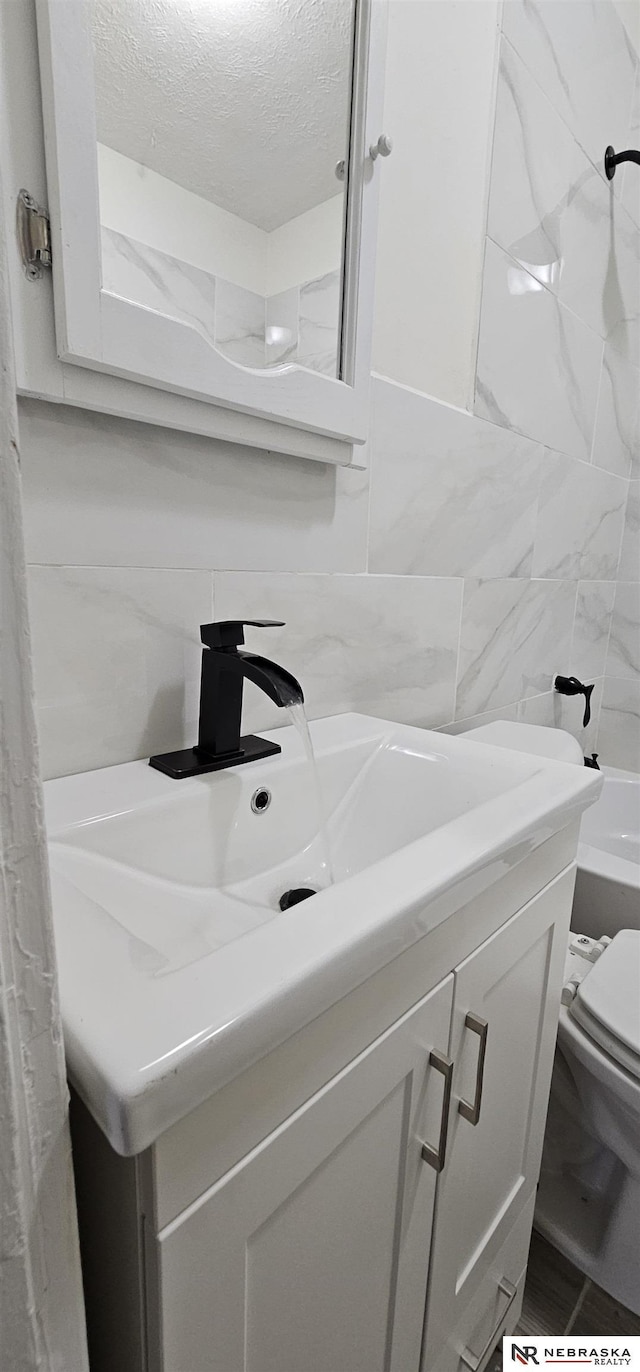 bathroom with vanity, toilet, a textured ceiling, tile walls, and tasteful backsplash