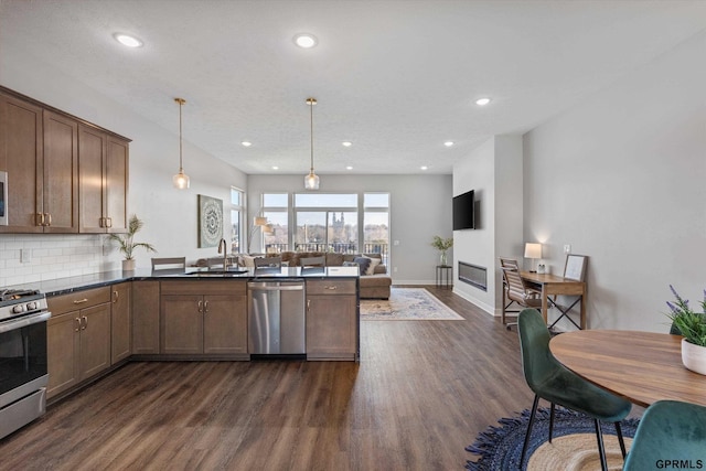 kitchen with sink, hanging light fixtures, dark hardwood / wood-style flooring, kitchen peninsula, and stainless steel appliances