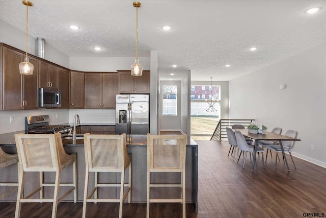 kitchen featuring appliances with stainless steel finishes, dark wood-style flooring, dark brown cabinets, and tasteful backsplash