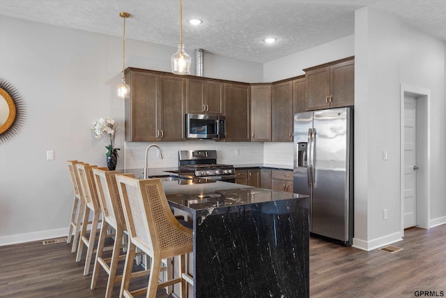 kitchen featuring decorative backsplash, appliances with stainless steel finishes, a sink, dark stone countertops, and a peninsula