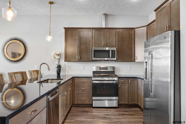 kitchen featuring a peninsula, a sink, appliances with stainless steel finishes, dark wood-style floors, and tasteful backsplash