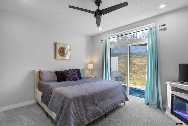 carpeted bedroom with baseboards, a glass covered fireplace, ceiling fan, access to outside, and a textured ceiling