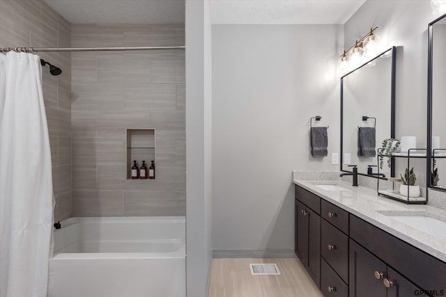 full bath with double vanity, shower / tub combo, baseboards, visible vents, and a sink