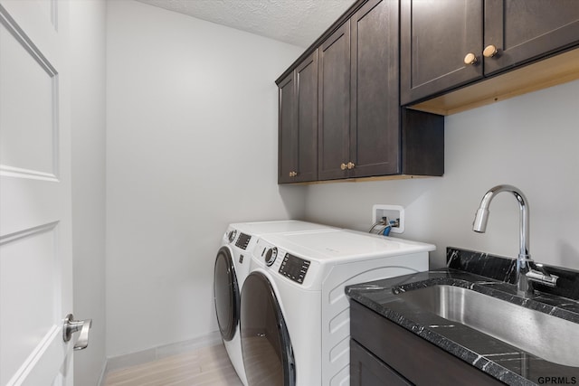 laundry room featuring cabinet space, a textured ceiling, light wood-style floors, separate washer and dryer, and a sink