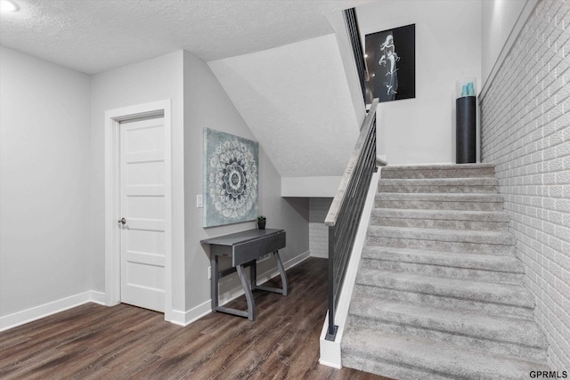 staircase with hardwood / wood-style floors, a textured ceiling, vaulted ceiling, and brick wall