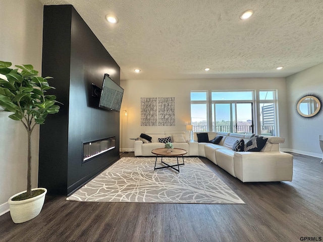 living area featuring wood finished floors, baseboards, a textured ceiling, a glass covered fireplace, and recessed lighting
