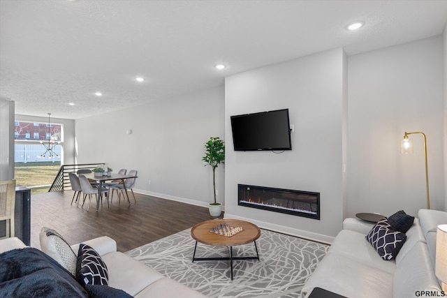 living room featuring baseboards, a glass covered fireplace, wood finished floors, a textured ceiling, and recessed lighting