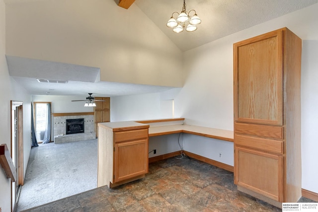 unfurnished office featuring a tile fireplace, dark colored carpet, vaulted ceiling, built in desk, and ceiling fan with notable chandelier