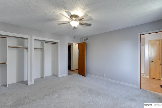 unfurnished bedroom featuring light carpet, a textured ceiling, ceiling fan, and multiple closets