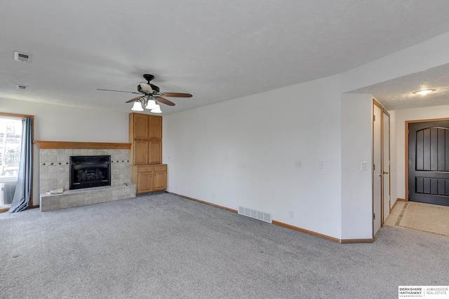 unfurnished living room featuring light carpet, a textured ceiling, ceiling fan, and a tiled fireplace