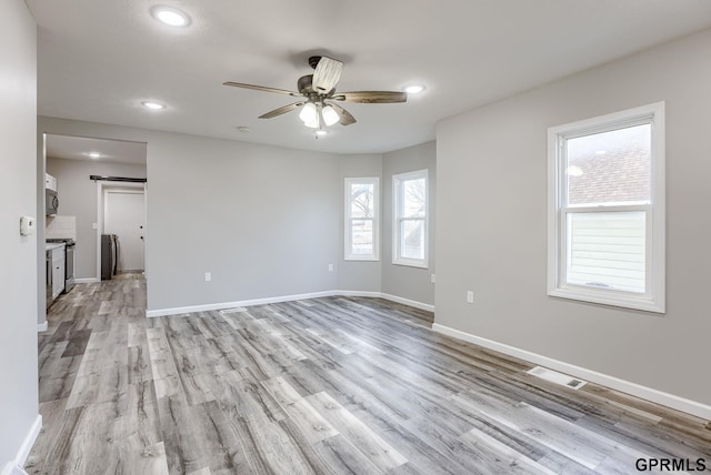 empty room with ceiling fan, a barn door, washer / dryer, and light wood-type flooring