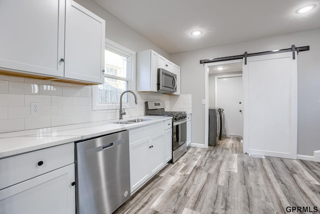 kitchen with appliances with stainless steel finishes, light wood-type flooring, sink, a barn door, and white cabinetry