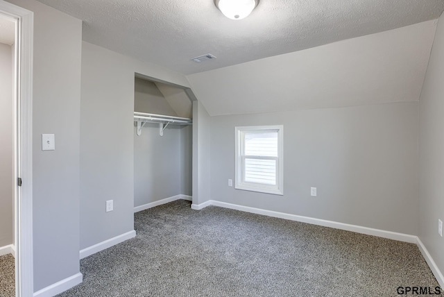 unfurnished bedroom with carpet flooring, a closet, a textured ceiling, and vaulted ceiling