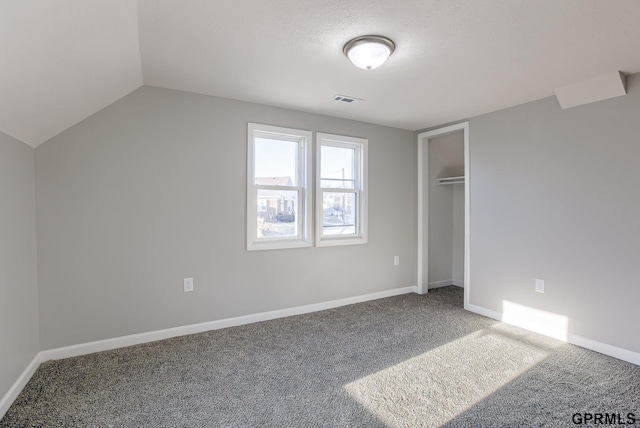 unfurnished bedroom featuring carpet, a closet, a textured ceiling, and vaulted ceiling