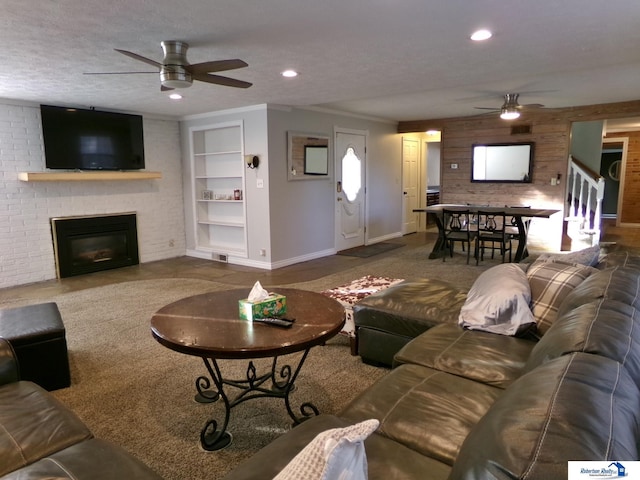 living room featuring ceiling fan, a fireplace, wood walls, and a textured ceiling