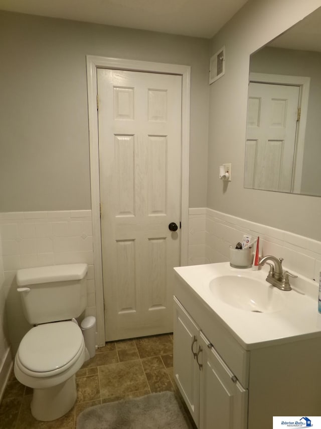 bathroom featuring vanity, tile walls, and toilet