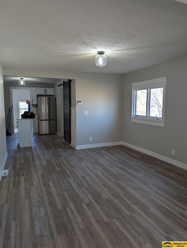 unfurnished living room with a barn door, dark wood-type flooring, and a textured ceiling