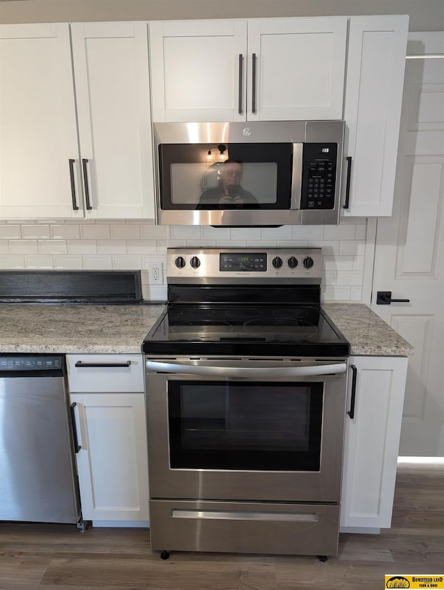 kitchen with appliances with stainless steel finishes, backsplash, dark hardwood / wood-style flooring, light stone counters, and white cabinets