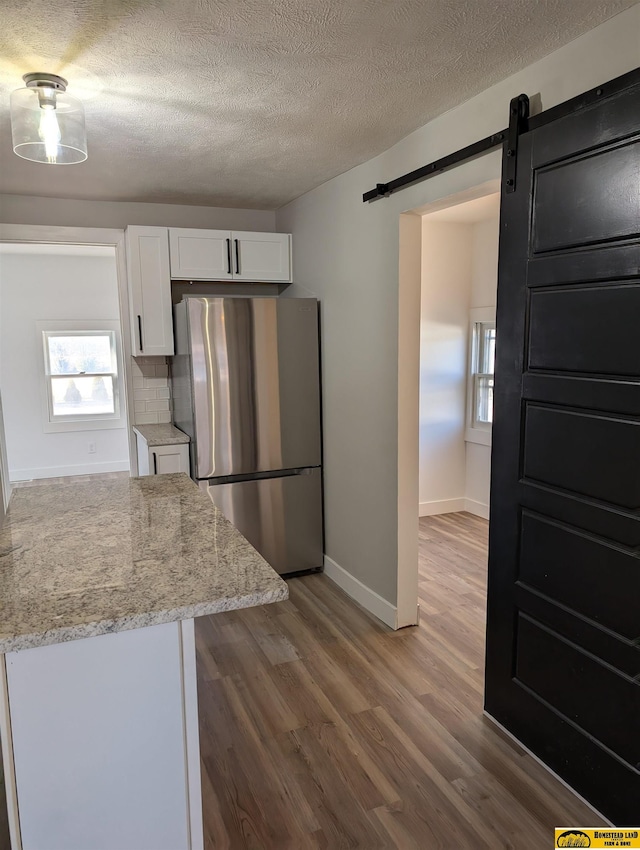 kitchen featuring light stone countertops, stainless steel fridge, a barn door, and white cabinetry