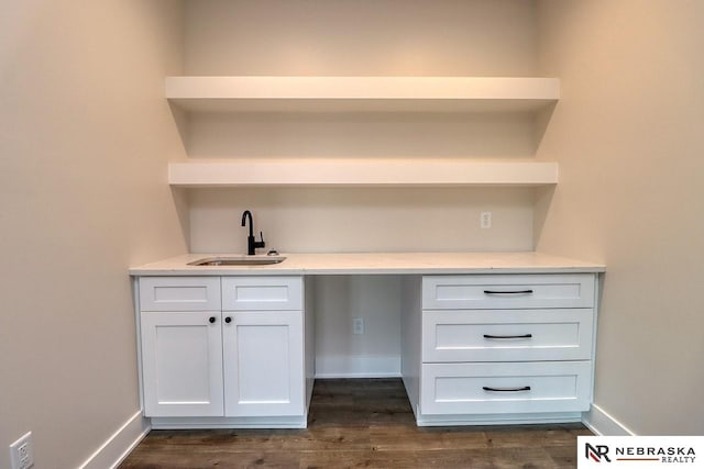 bar featuring dark hardwood / wood-style flooring, white cabinetry, sink, and built in desk