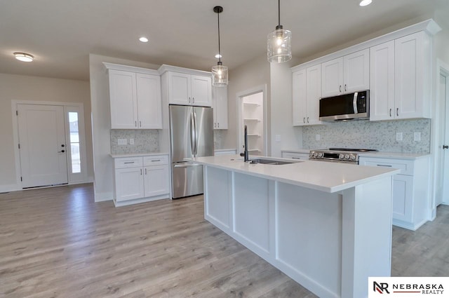 kitchen with sink, hanging light fixtures, a kitchen island with sink, white cabinets, and appliances with stainless steel finishes