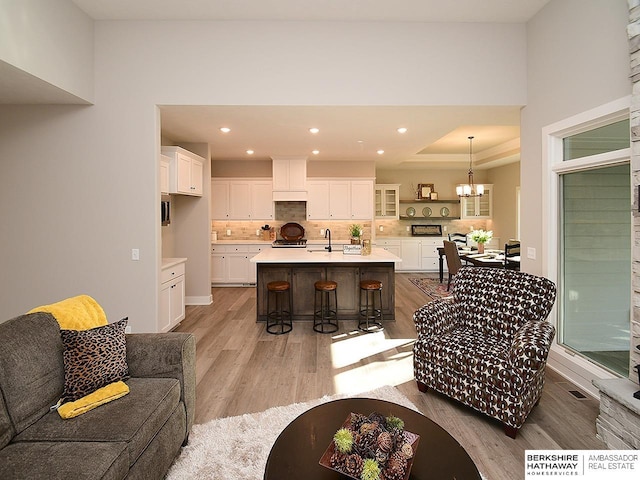 living room featuring a notable chandelier, sink, a tray ceiling, and light hardwood / wood-style flooring