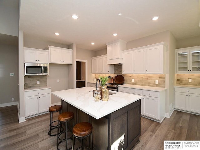 kitchen featuring white cabinetry, a center island with sink, light stone counters, and dark hardwood / wood-style floors