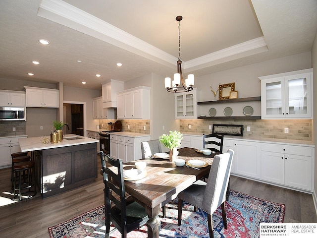 dining room featuring dark hardwood / wood-style flooring, ornamental molding, a raised ceiling, sink, and an inviting chandelier