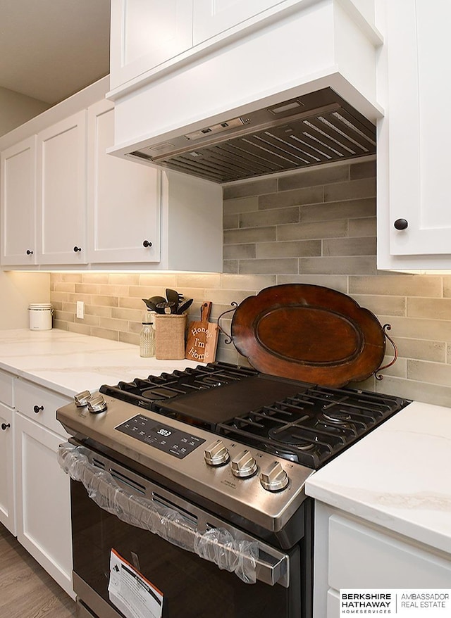 kitchen featuring decorative backsplash, light stone counters, custom exhaust hood, high end stainless steel range, and white cabinets