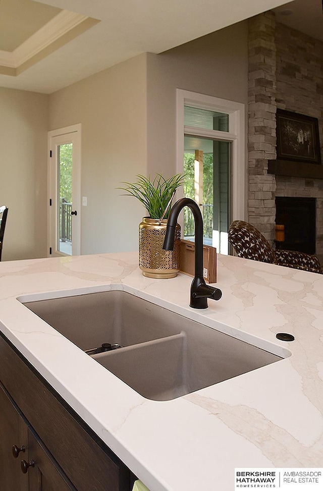 interior space with light stone countertops, dark brown cabinetry, a stone fireplace, and sink