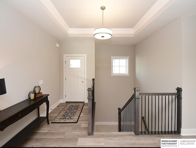 foyer entrance with light hardwood / wood-style flooring, a raised ceiling, and crown molding