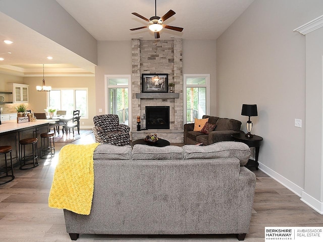 living room featuring a stone fireplace, hardwood / wood-style floors, a healthy amount of sunlight, and ceiling fan with notable chandelier