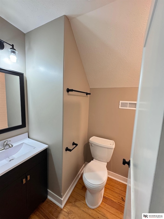 bathroom featuring hardwood / wood-style floors, vanity, lofted ceiling, toilet, and a textured ceiling