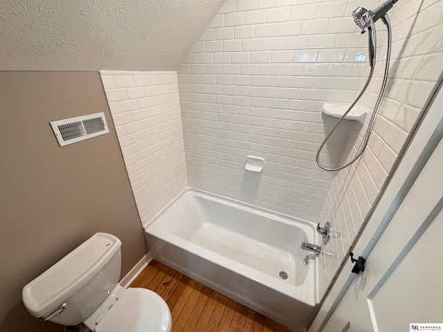 bathroom with a textured ceiling, hardwood / wood-style floors, toilet, tiled shower / bath, and lofted ceiling