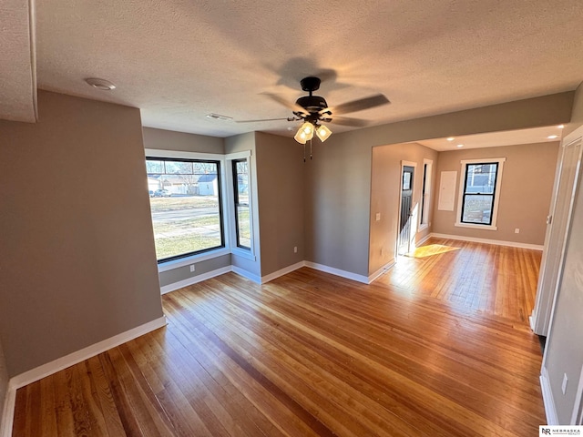 empty room with a textured ceiling, light wood-type flooring, and ceiling fan