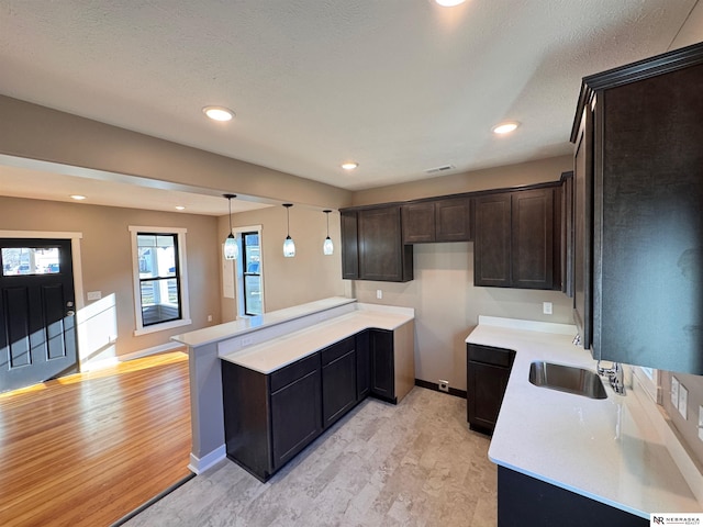 kitchen with kitchen peninsula, decorative light fixtures, light hardwood / wood-style floors, and sink