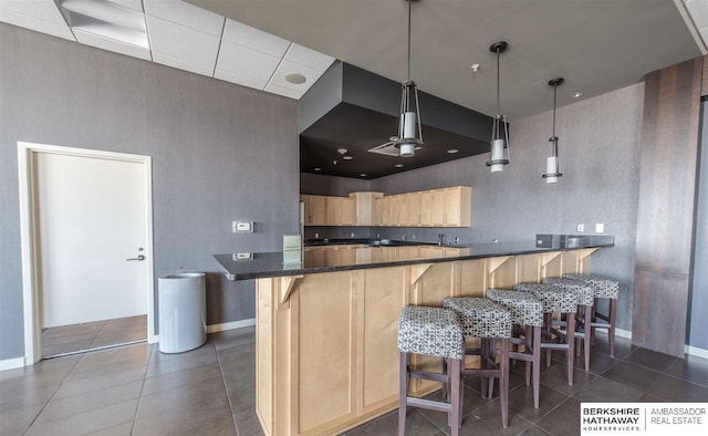 kitchen featuring dark tile patterned flooring, a kitchen breakfast bar, light brown cabinetry, decorative light fixtures, and kitchen peninsula