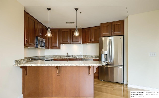 kitchen featuring light hardwood / wood-style flooring, decorative light fixtures, light stone counters, kitchen peninsula, and stainless steel appliances